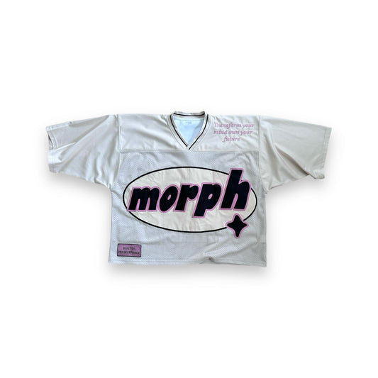 A cream mesh jersey with pink detailing along the sleeves, featuring a large oval-shaped logo on the front that reads “morph” in bold. The phrase “Transform your mind own your future” is placed in the upper right corner. The phrase “Built on Perseverance” is placed on a woven label in the lower left corner. 